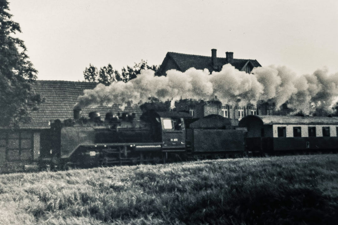 Rauchende Dampflok vor Bahnhofgebäude. Foto in schwarz weiss